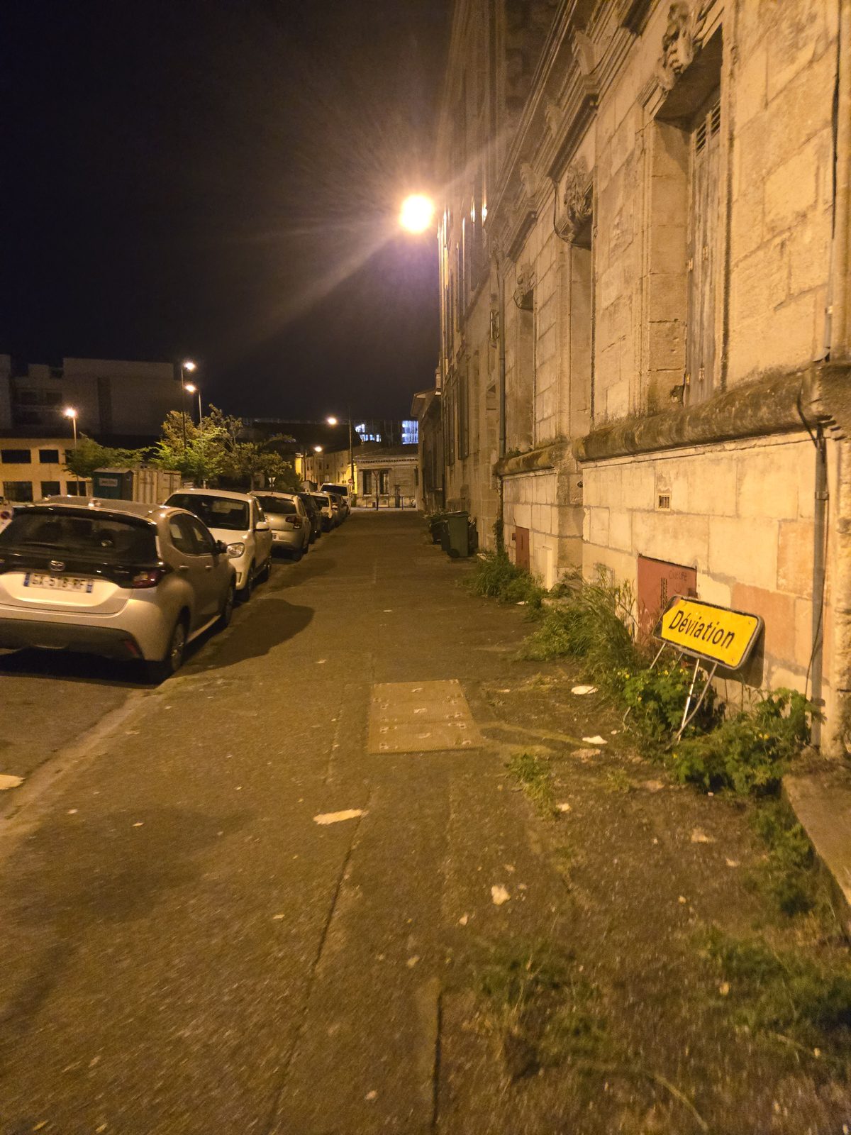 A dark Bordeaux street with crumbling facades and graffiti near the station